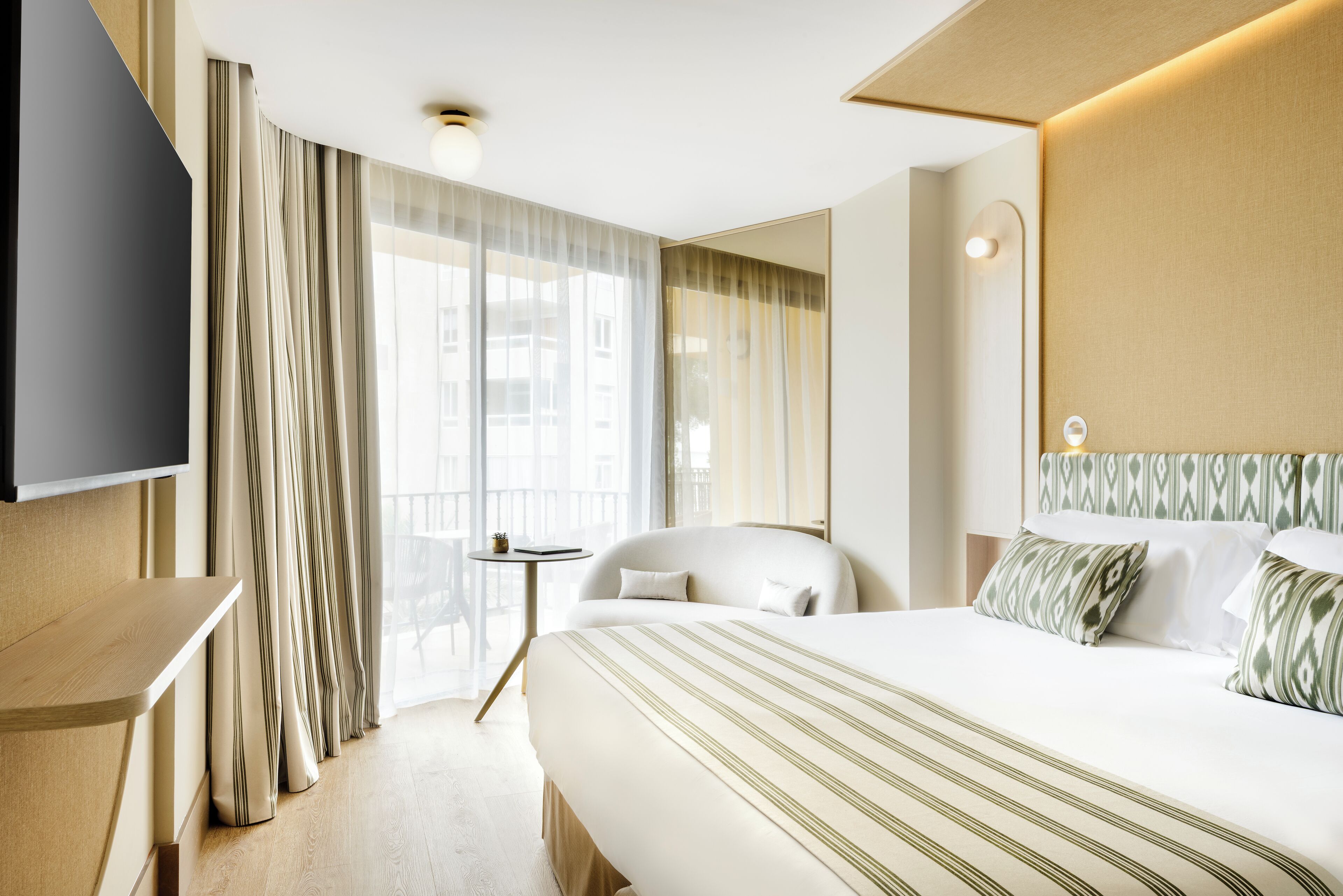 A hotel room with a large bed, a TV mounted on the wall, a small table, and a chair.