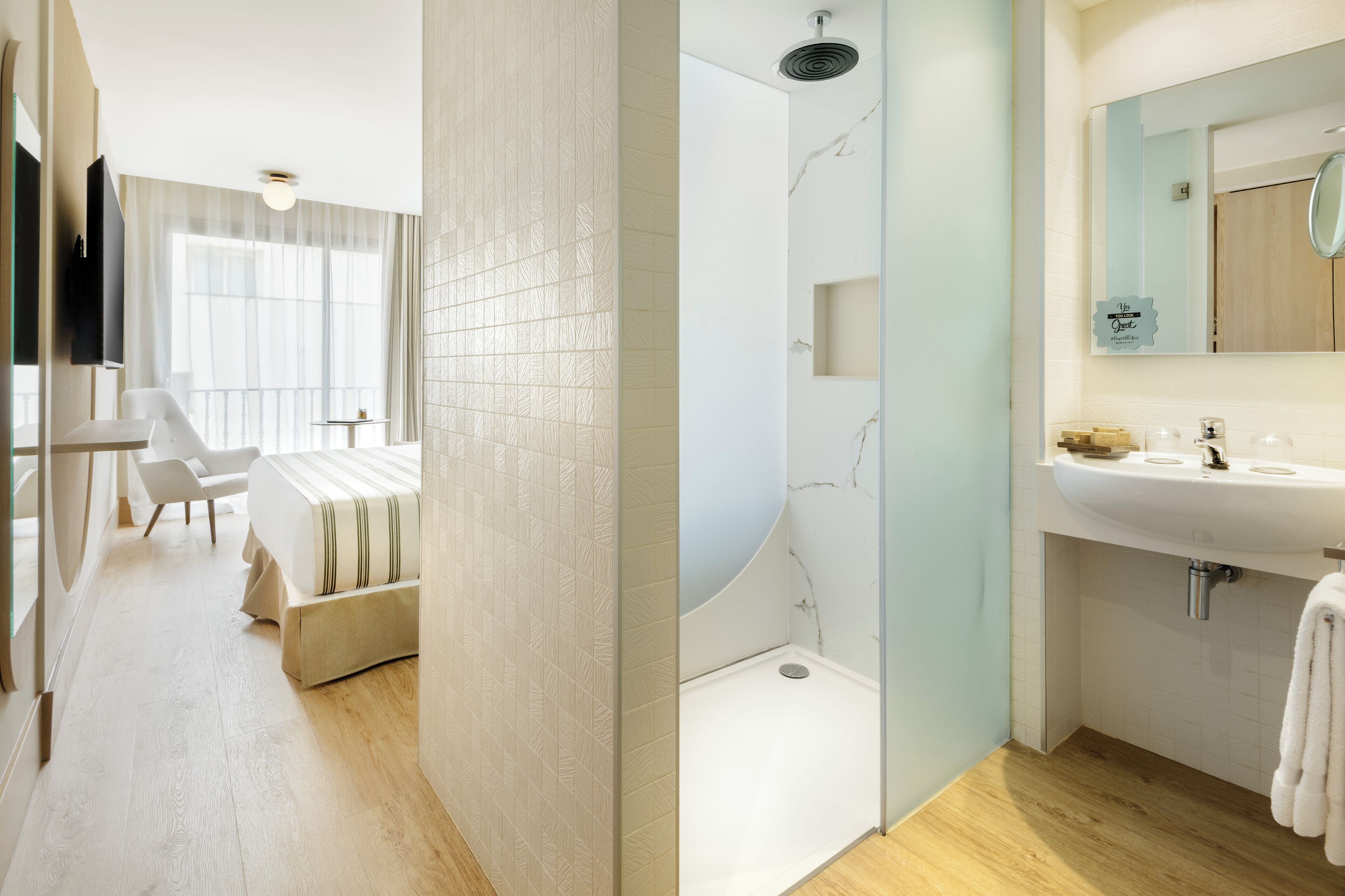 Habitación de hotel moderna con cama, ducha, tocador con espejo y vistas al exterior.