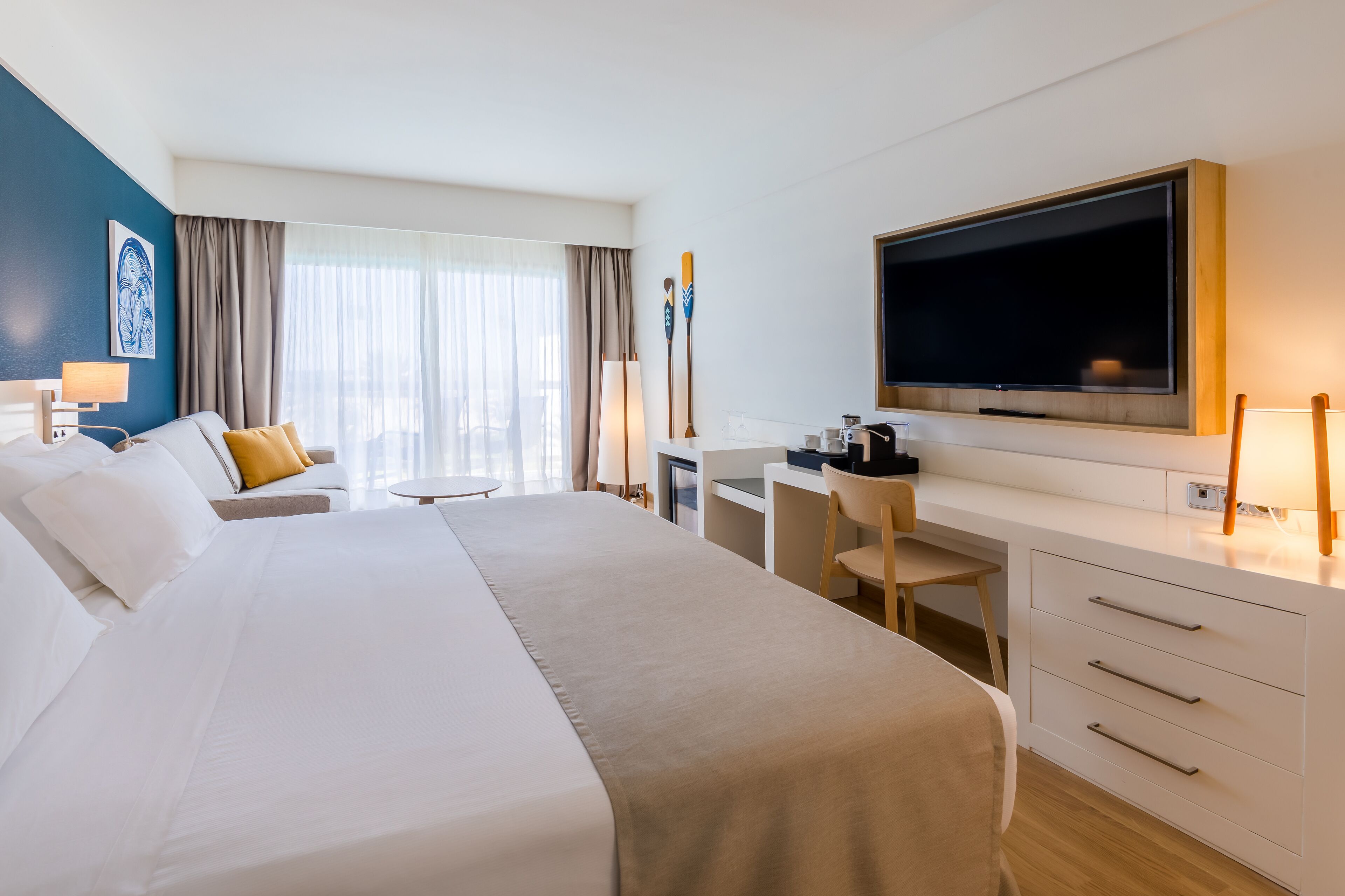 A hotel room with a large bed, a desk with a chair, a television, and a window with curtains.