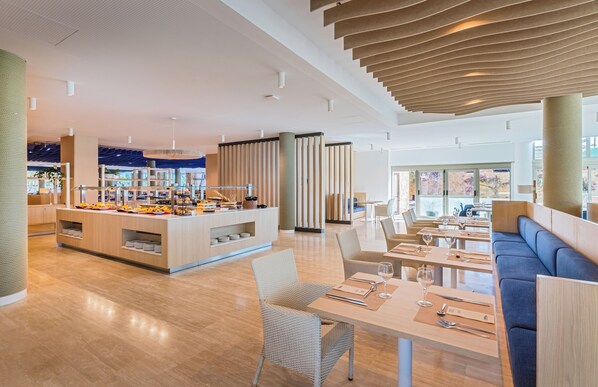 A modern restaurant with a central buffet, seating areas, and a high ceiling with unique lighting. - Barceló Fuerteventura Mar (Antigua)