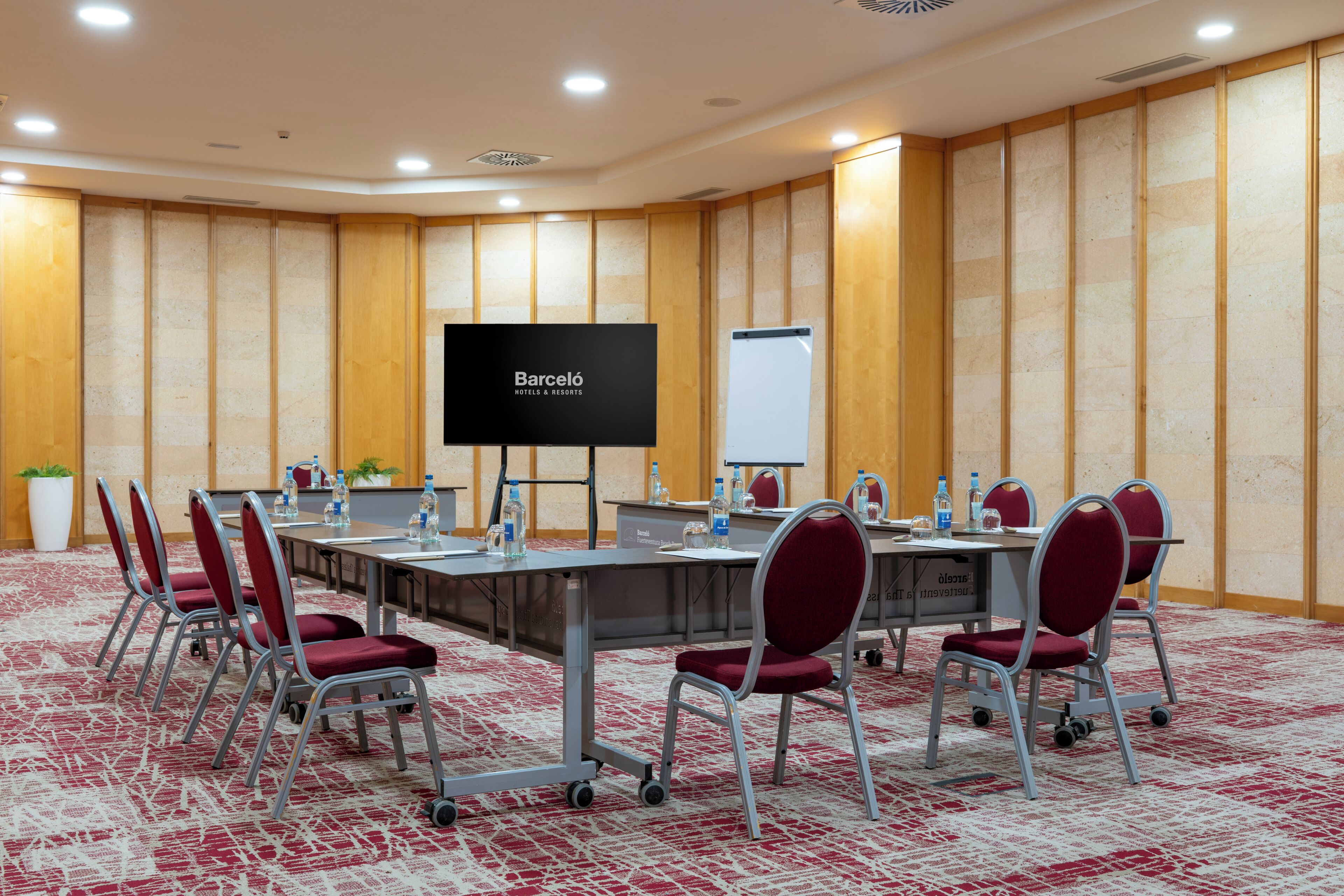 A conference room with a long table, red chairs, a screen displaying 'Barceló Hotels & Resorts', and a whiteboard.