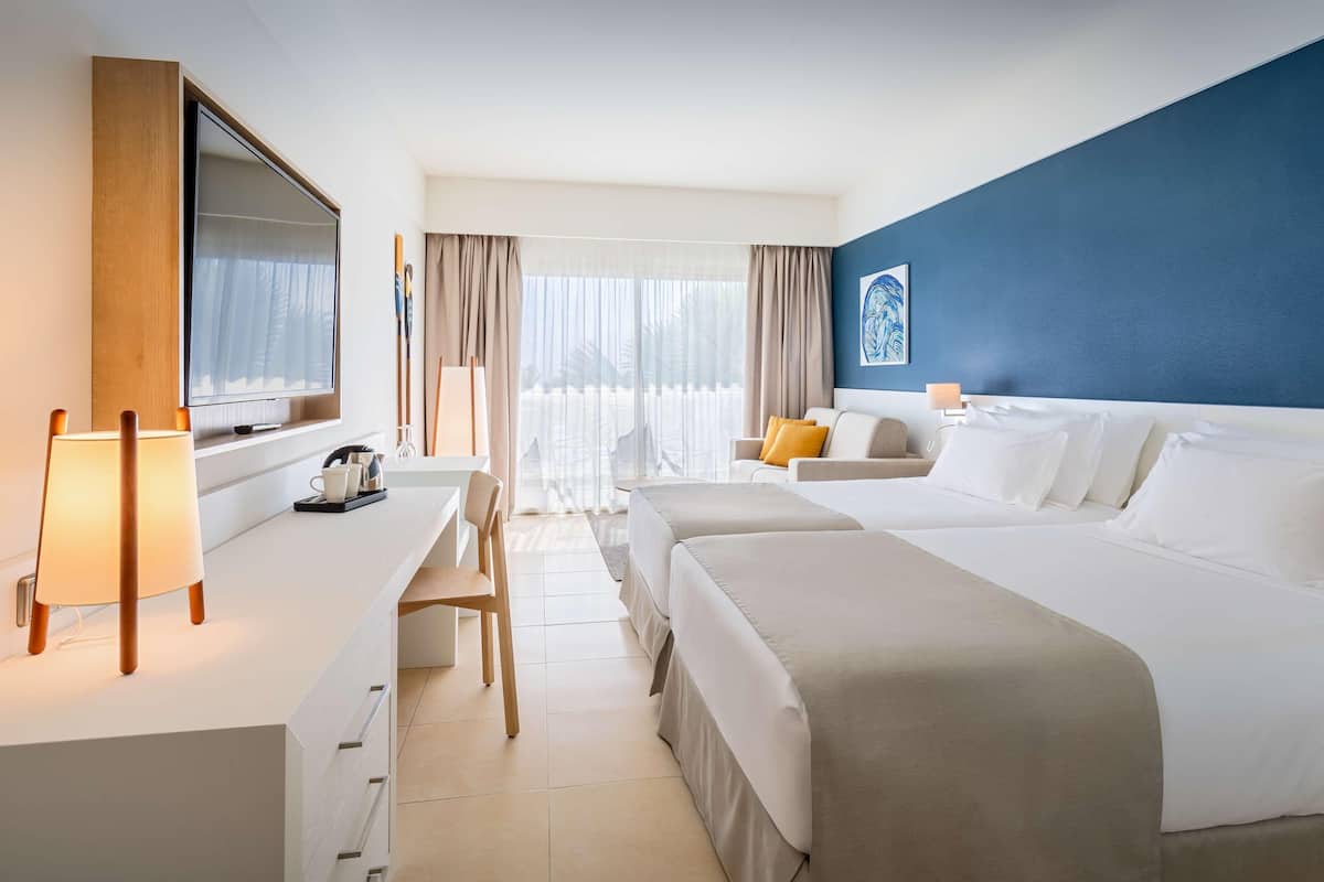Une chambre d’hôtel avec un grand lit, un bureau avec une lampe, une télévision et une vue sur l’extérieur.