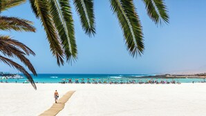 Una playa con un paseo de madera, palmeras y sombrillas.