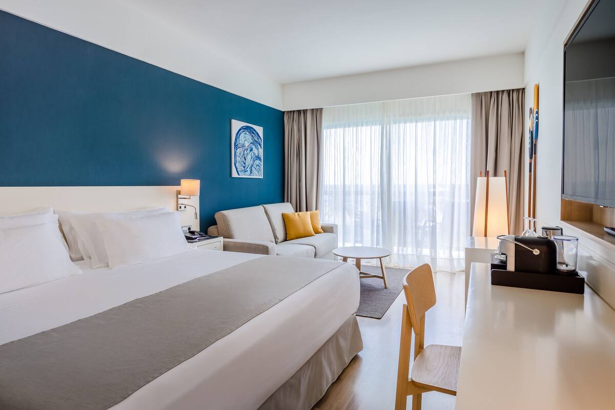 A hotel room with a large bed, a sofa, a desk, and a TV.