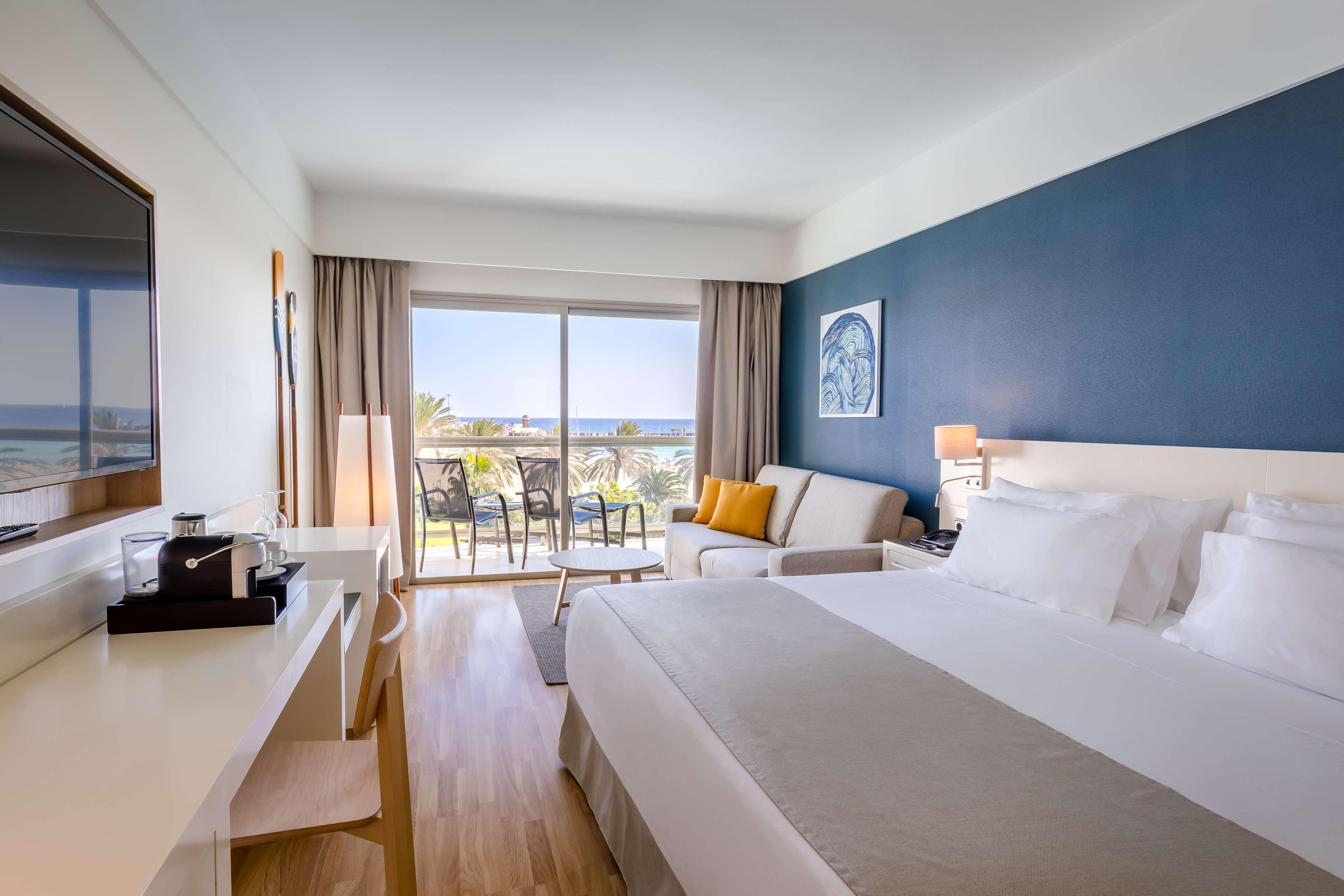 Une chambre d’hôtel comprenant un lit, un bureau, une chaise, une télévision, une fenêtre avec vue et un balcon.