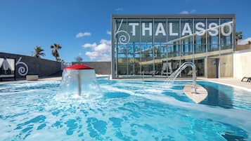 Un área de piscina moderna con un edificio de cristal al fondo, que dice "THALASSO".