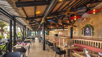An outdoor restaurant with wooden tables and chairs, stone walls, and hanging red lights.
