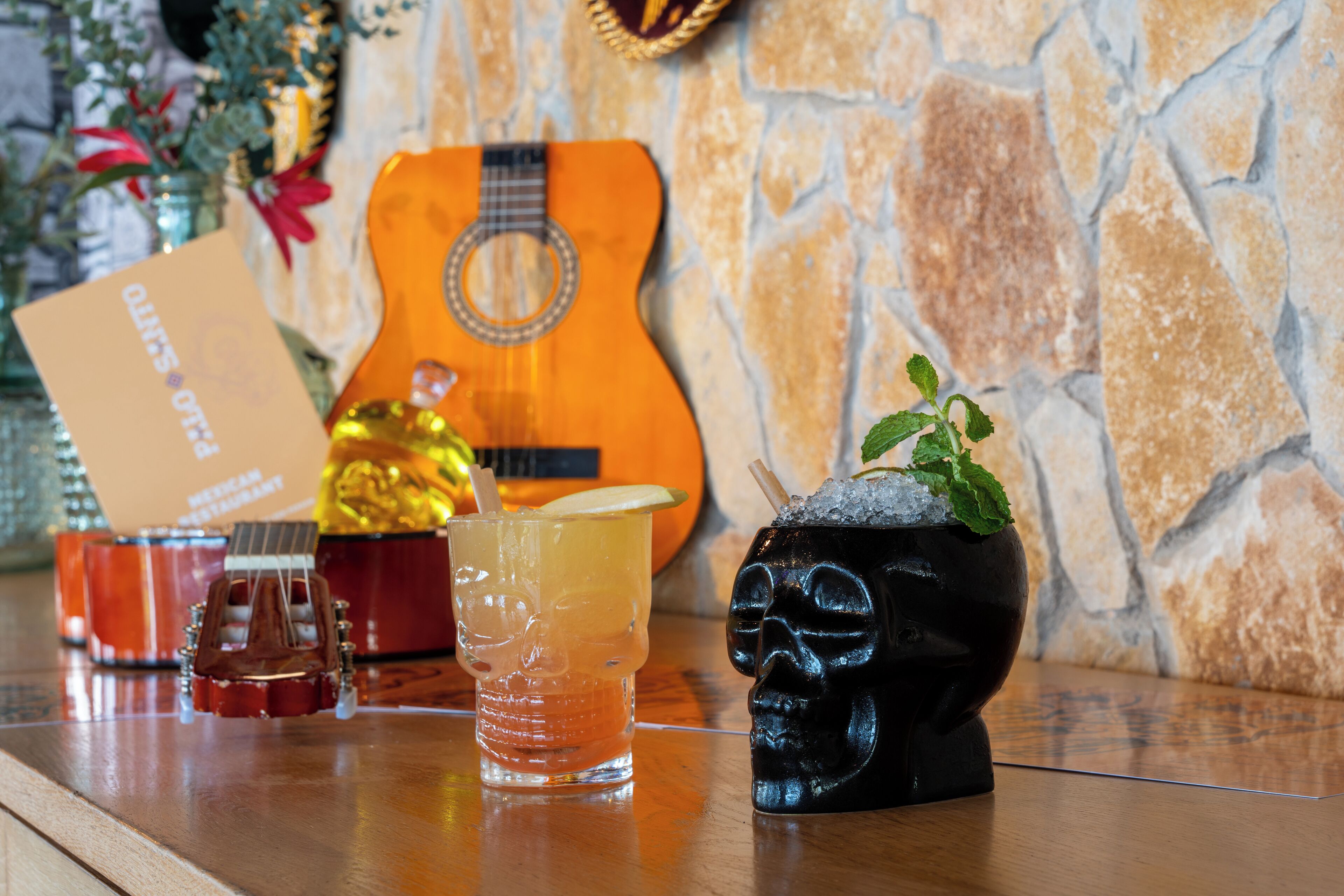 A bar area with a guitar, drinks, and a skull-shaped cocktail glass.