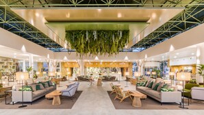 Un vestíbulo amplio con mobiliario moderno, una zona de estar central y plantas colgantes.