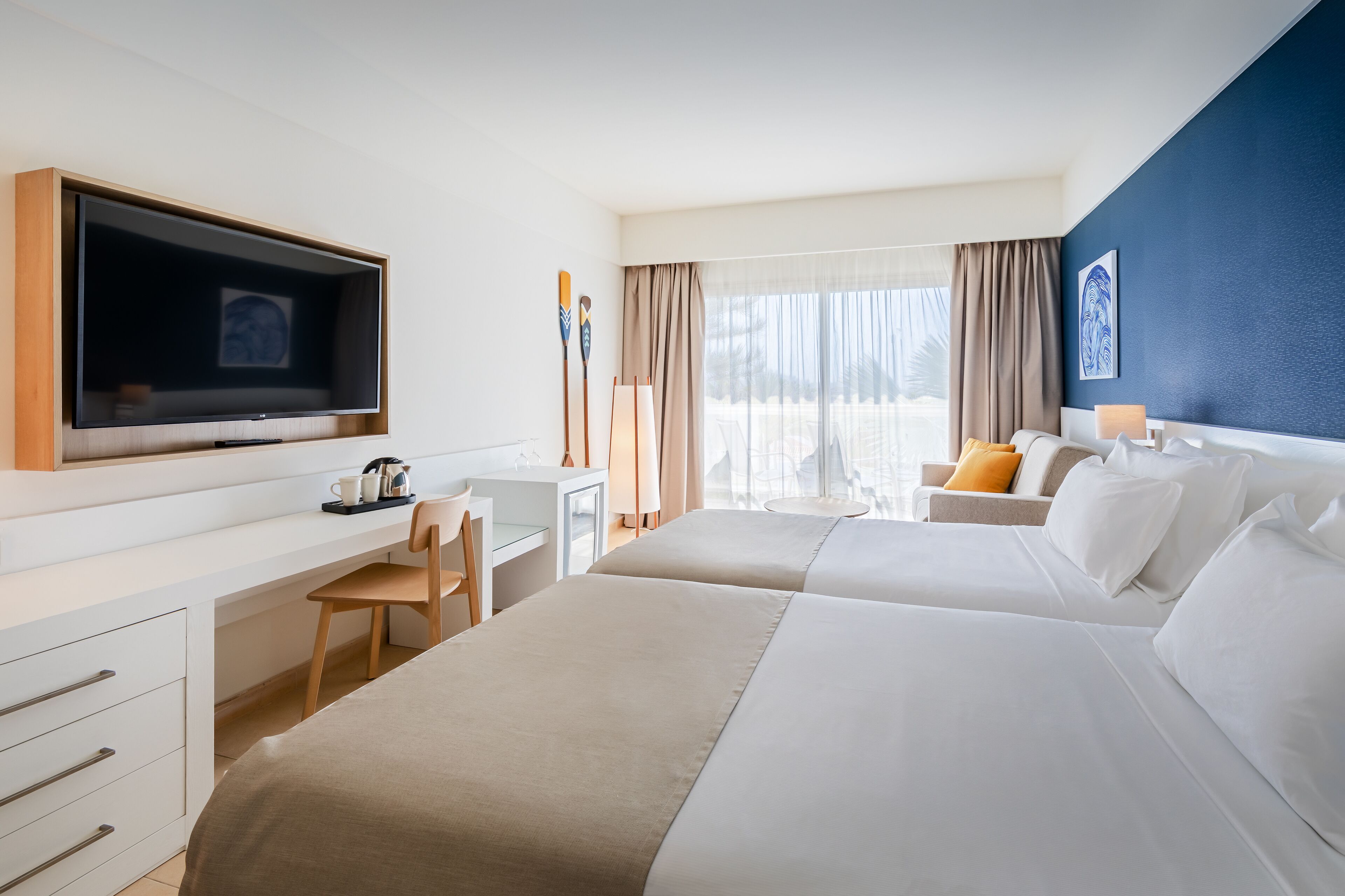 A hotel room with a large bed, a desk with a chair, a television, and a view of the outdoors.