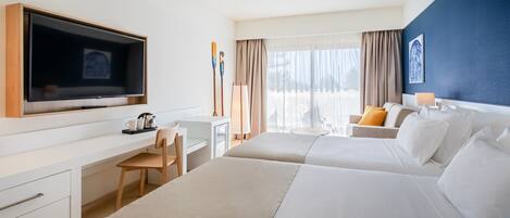 A hotel room with a large bed, a desk with a chair, a television, and a view of the outdoors.