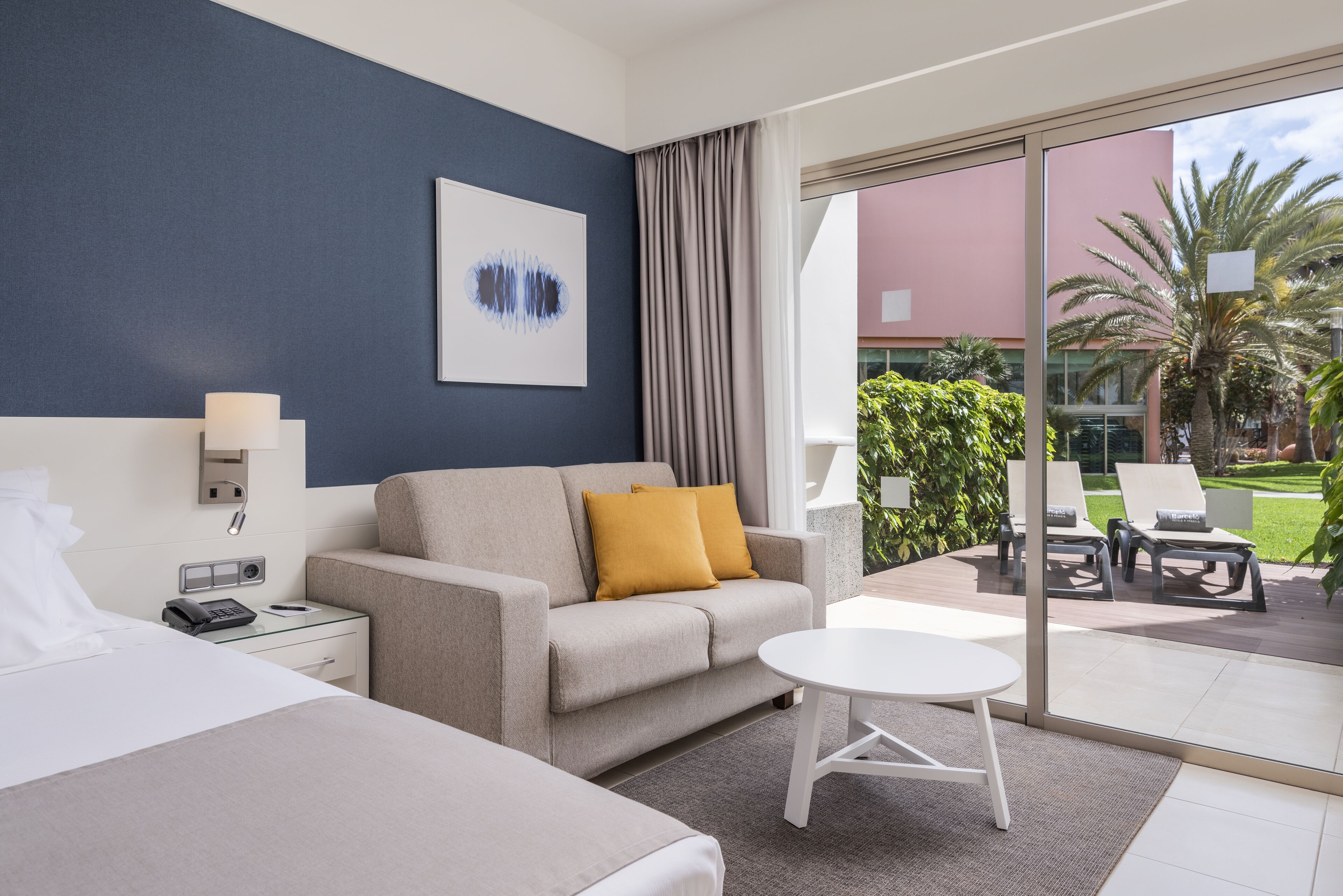 A hotel room with a bed, a sofa, a small table, and a view of the outdoor patio area.