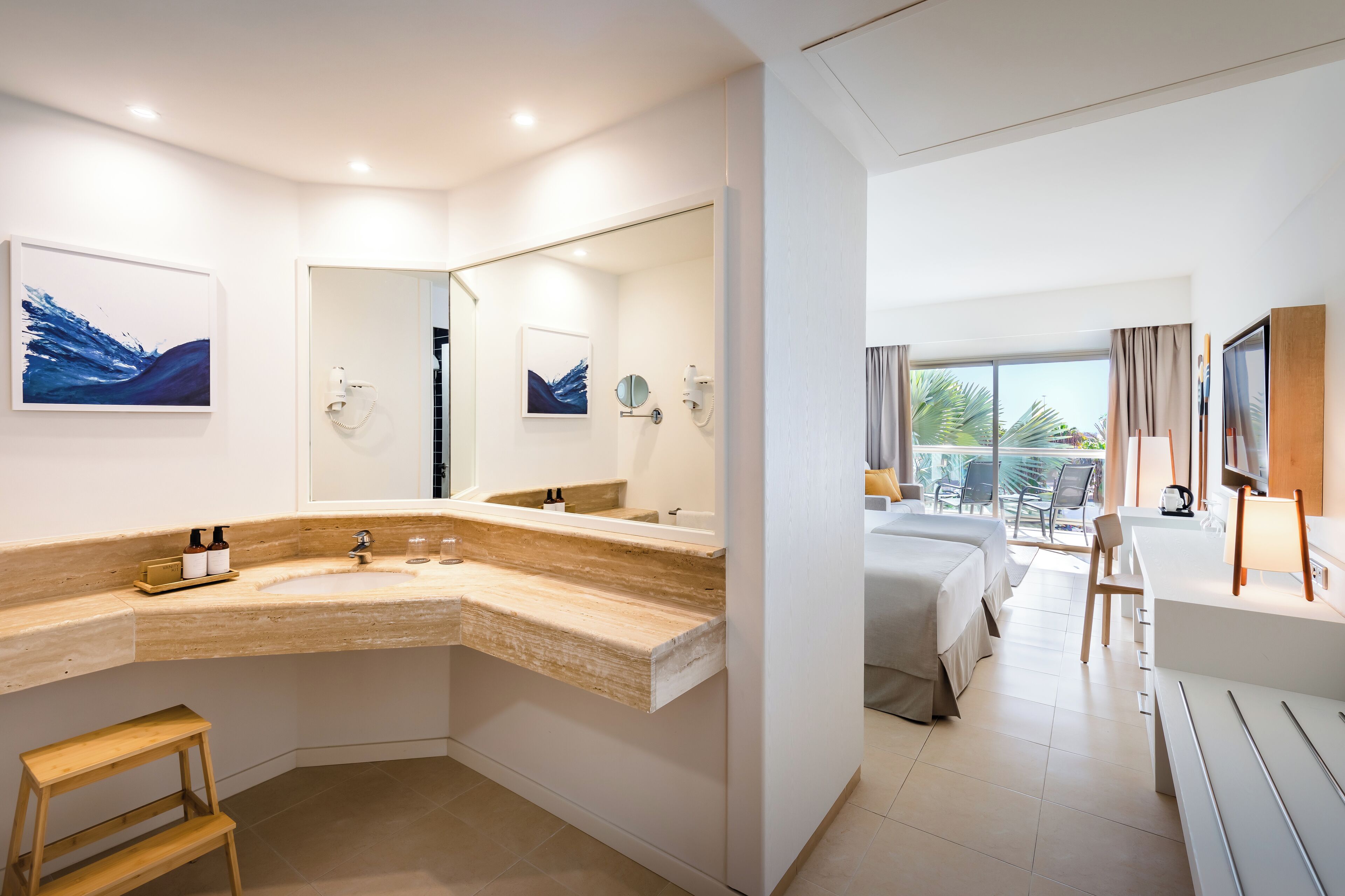 A modern bathroom with a curved sink, a wooden stool, and a large mirror.