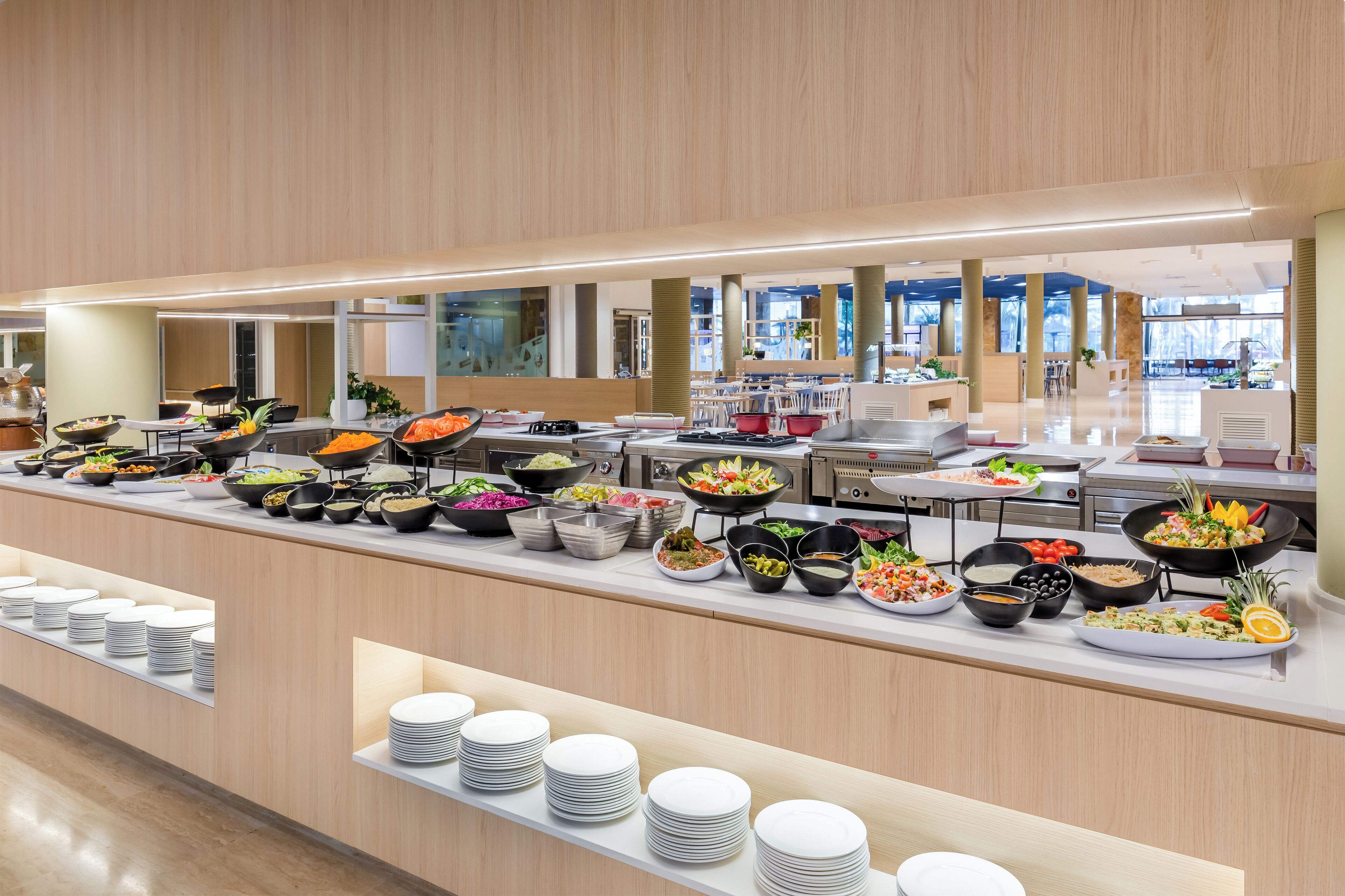 A buffet with various food items and stacked white plates.