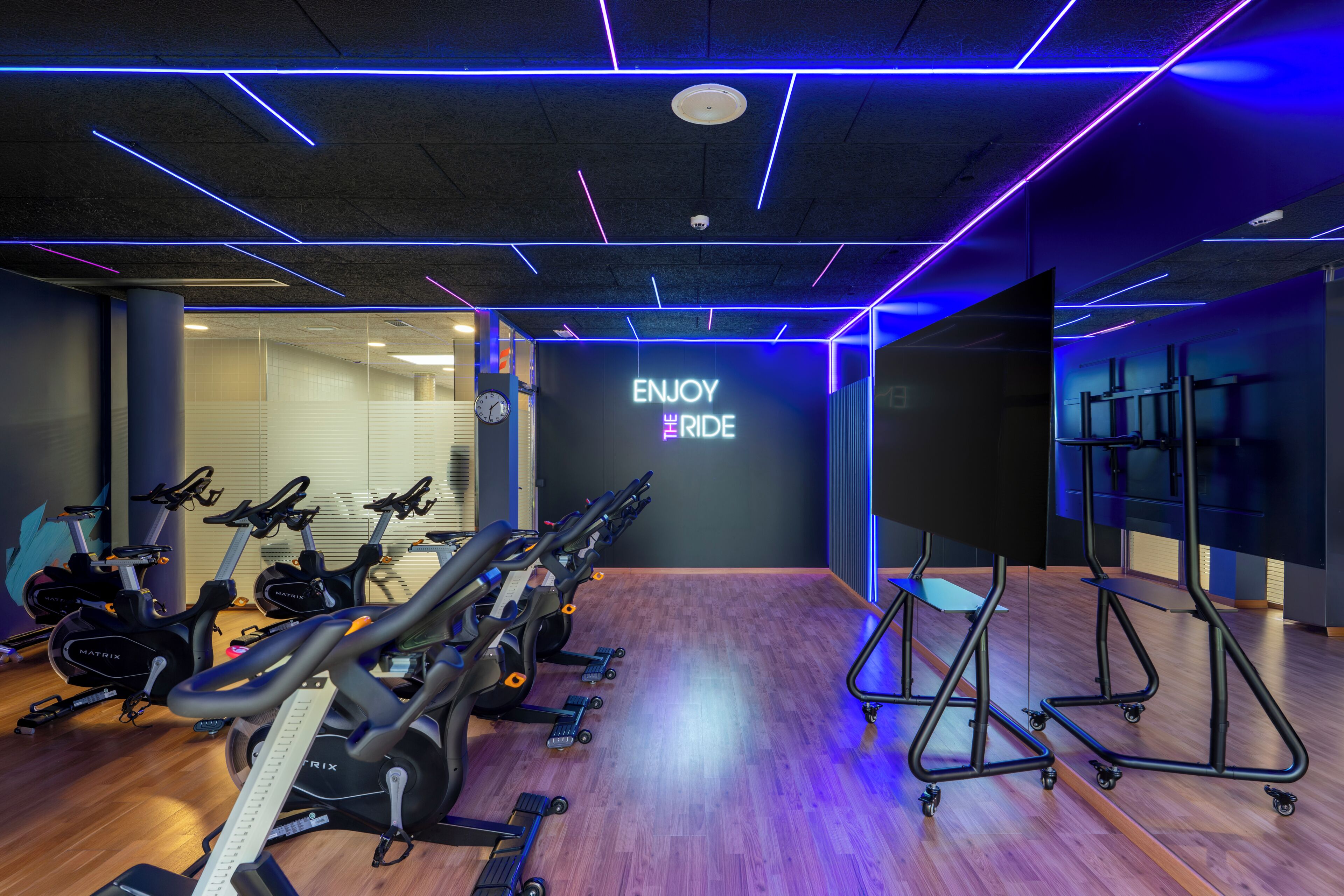 Academia com bicicletas ergométricas, esteiras e uma parede com a inscrição 'ENJOY THE RIDE'.