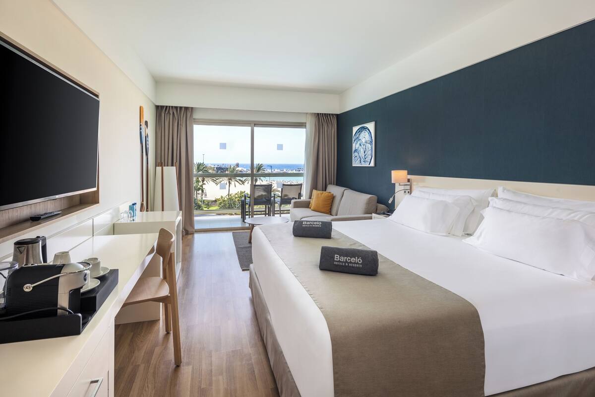 A hotel room with a bed, a desk, a chair, a television, and a view of the outdoors.