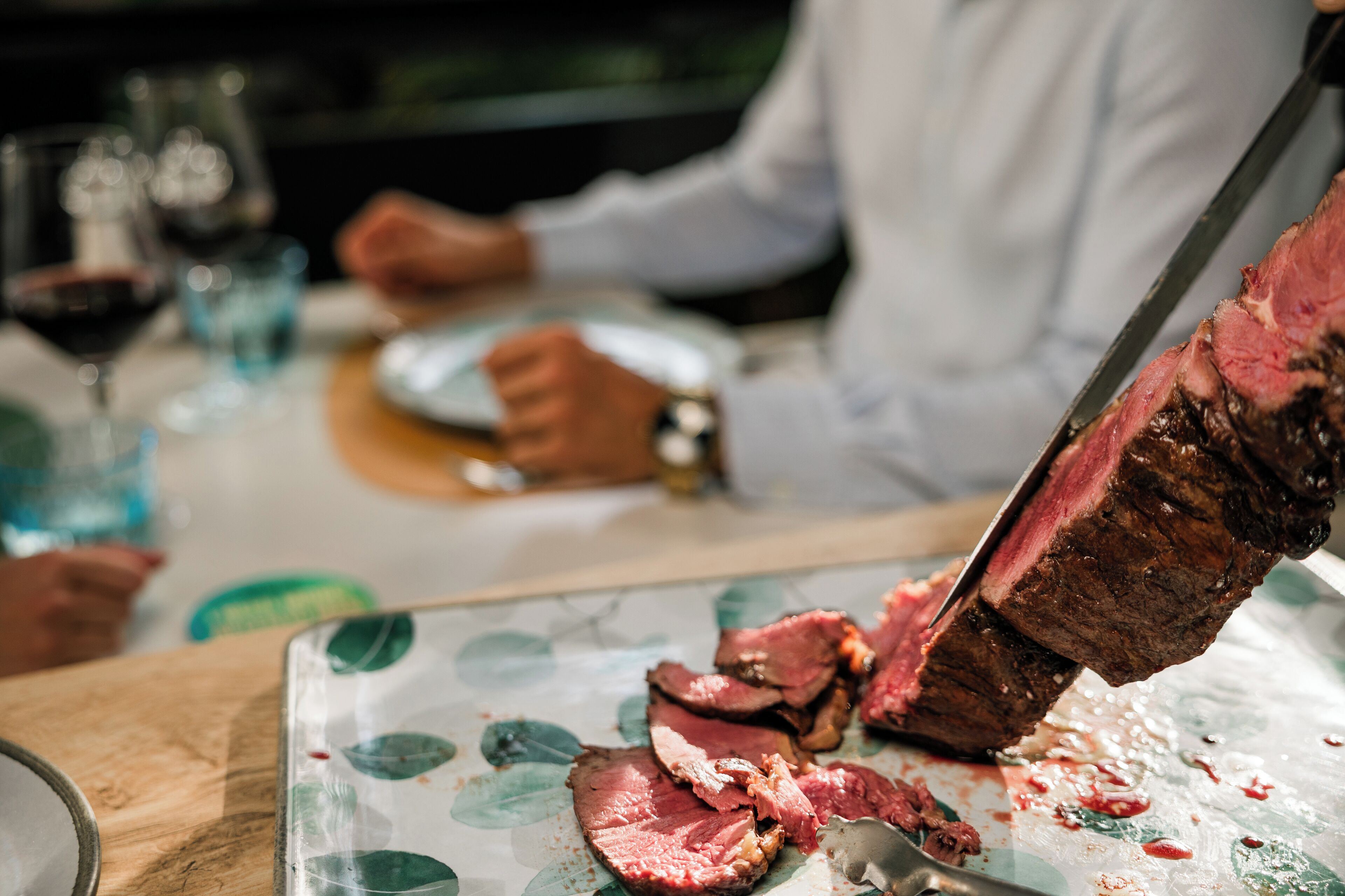 Primer plano de un bistec siendo cortado, con un cuchillo y un plato sobre una mesa.