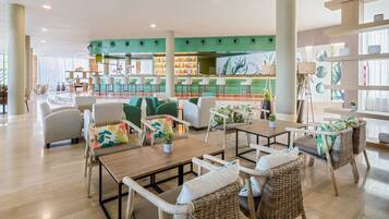 A modern lounge area with wicker furniture, a bar with stools, and a green accent wall.