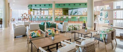 A modern lounge area with wicker furniture, a bar with stools, and a green accent wall.