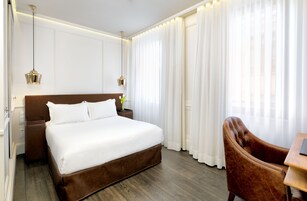 A hotel room with a large bed, a wooden nightstand, a brown leather chair, and a desk with a lamp.