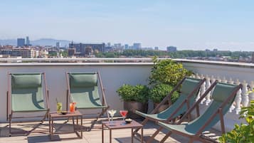 Una terraza en la azotea con cuatro sillones de descanso, una mesita con bebidas y plantas en macetas.