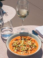 Uma mesa posta com uma tigela de sopa, um copo de vinho branco e um copo de água.