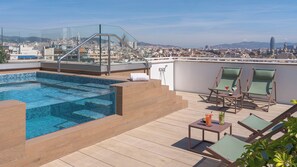 Une piscine sur le toit offrant une vue sur la ville, une balustrade en verre et des chaises longues.