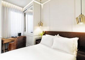 Quarto de hotel com cama, escrivaninha, cadeira, espelho e mesa de cabeceira com luminária.