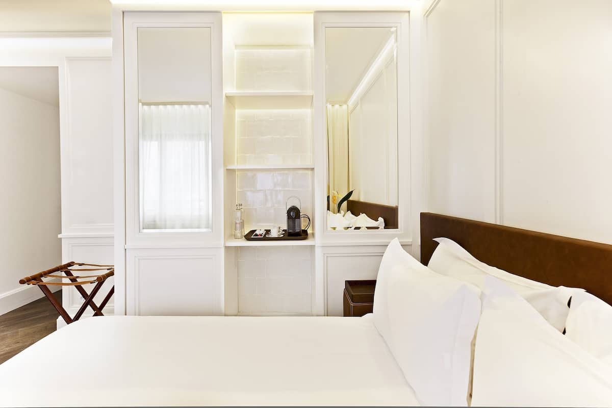 A hotel room with a large bed, a bedside table with a lamp, a mirror, and a built-in shelf with decorative items.