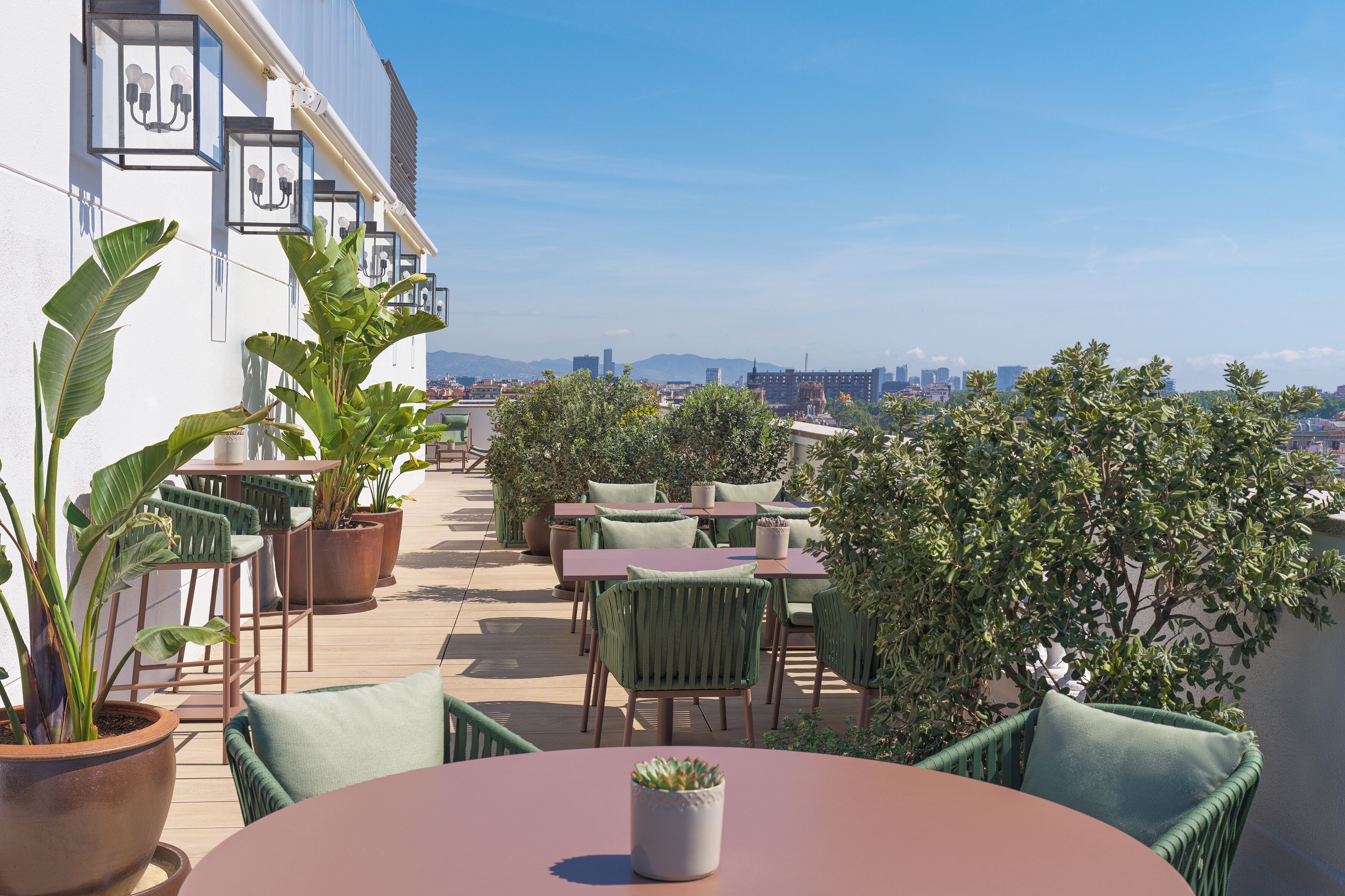 Un espacio al aire libre con mesas y sillas, plantas en macetas y vistas de la ciudad.