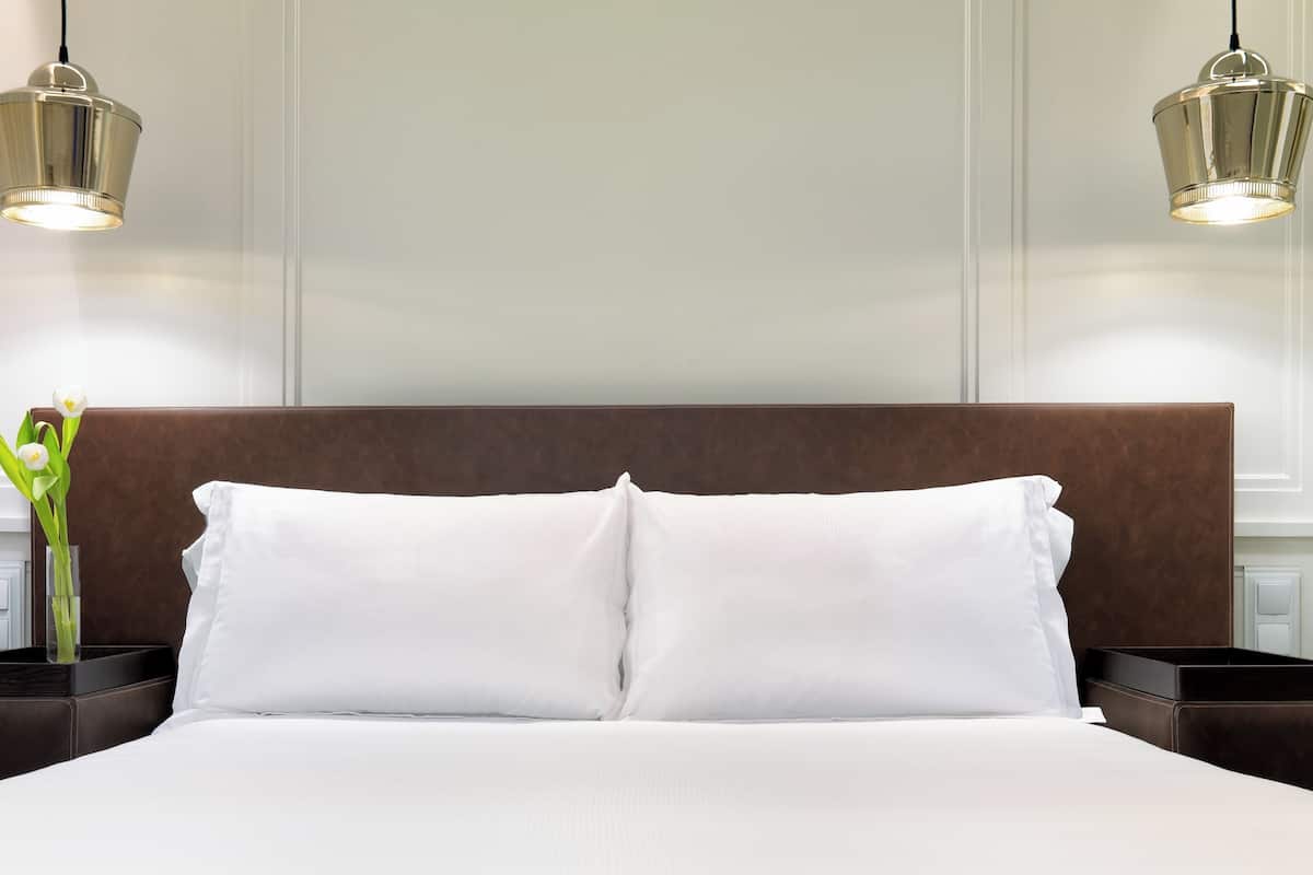 A neatly made bed with white linens, a brown headboard, and two bedside tables with lamps.