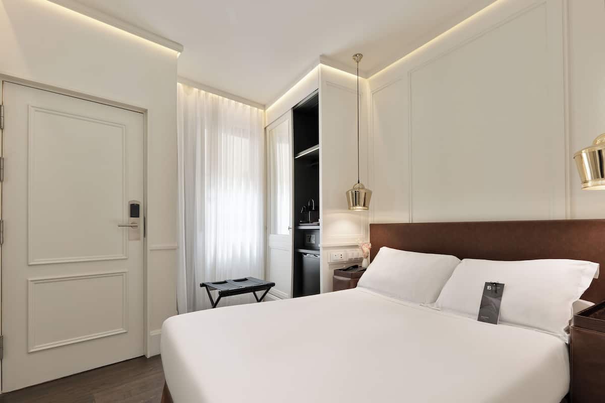 Une chambre d’hôtel avec un grand lit, une table de chevet, une commode, une armoire et une fenêtre avec des rideaux.