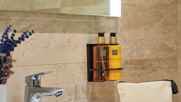 Een badkamer met een marmeren wand, een wastafel, twee glazen bekers en een fles Ritual of Mehr body lotion.