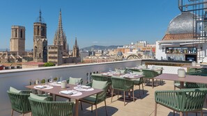 Une terrasse sur le toit, aménagée avec des tables et des chaises, un espace bar et une vue sur des bâtiments historiques.