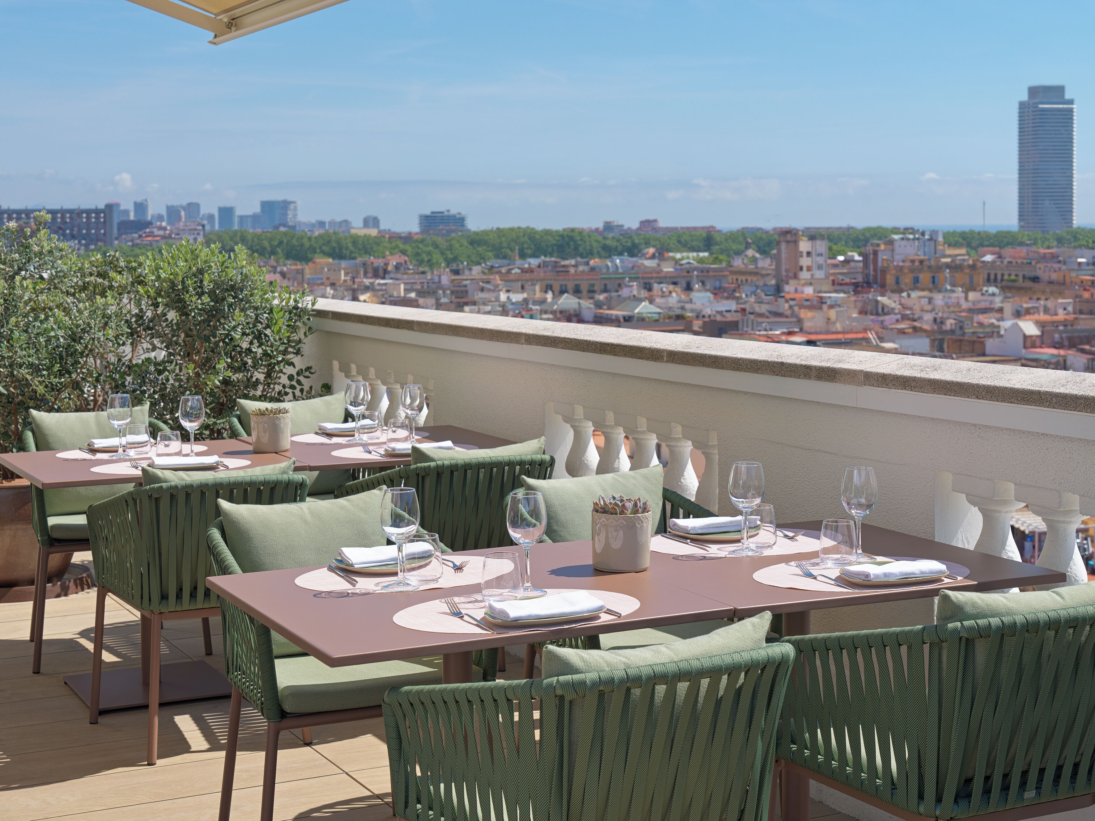 A rooftop restaurant with tables set for dining, overlooking a cityscape.