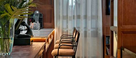 A wooden interior with a bar area, chairs, a bookshelf, and a large window with curtains.