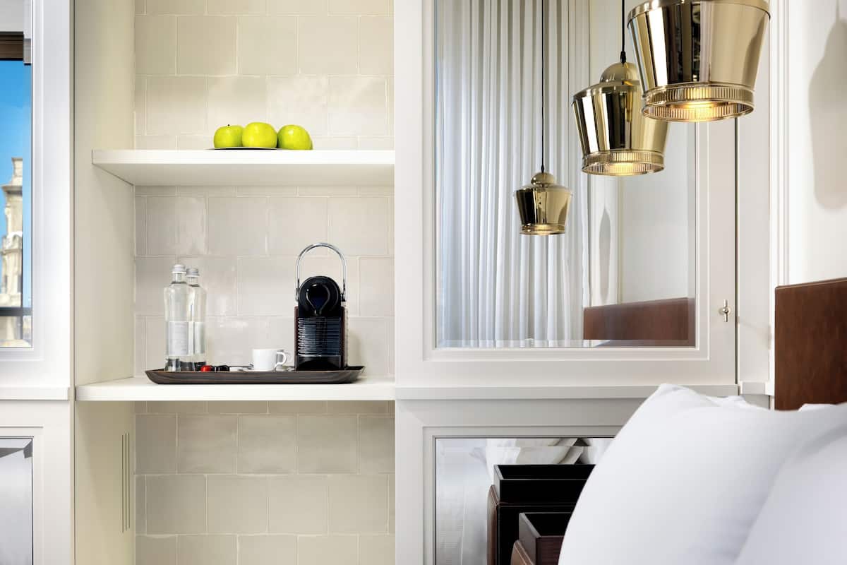 Une chambre d’hôtel équipée d’une kitchenette, d’un lit, d’une fenêtre avec des rideaux et d’un luminaire suspendu.