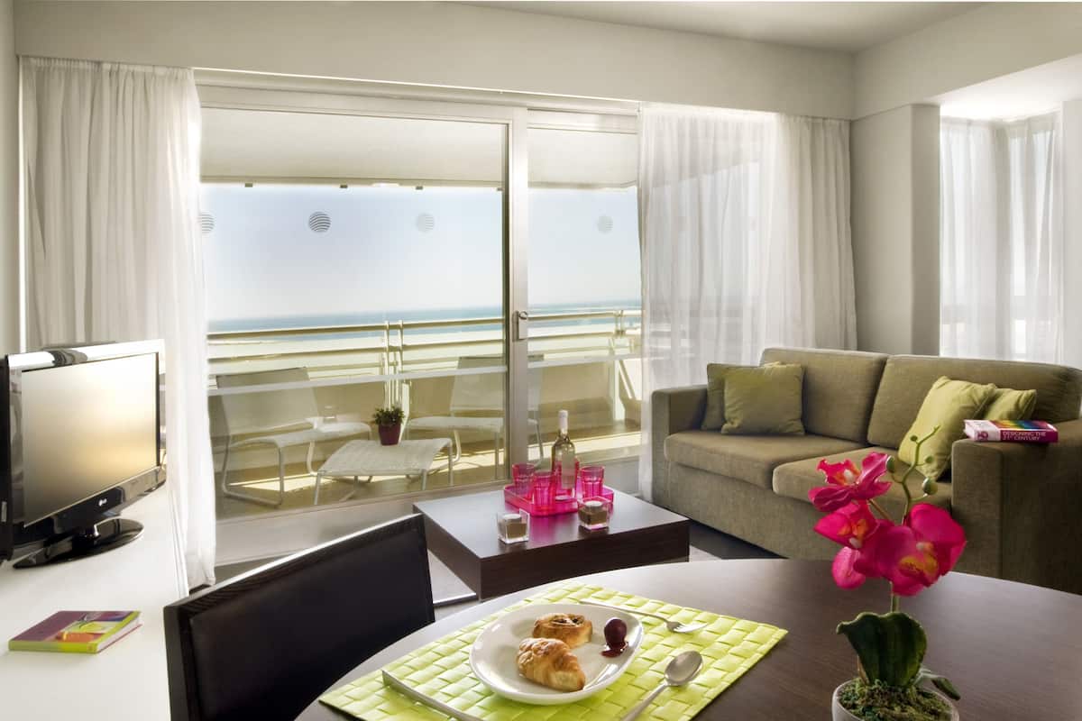 Una habitación de hotel con balcón, una mesa de comedor con un plato de comida, un sofá y un televisor.