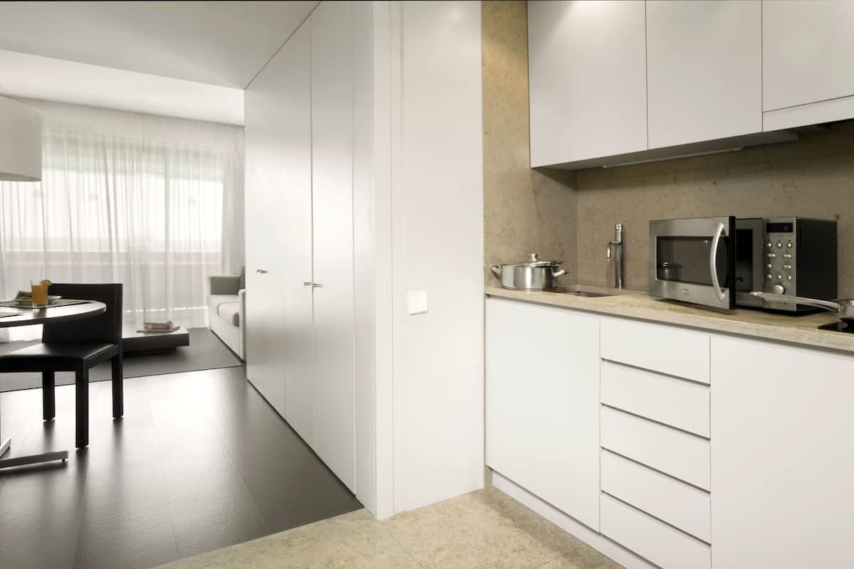 Una cocina moderna con armarios blancos, microondas y un lavamanos. Hay un comedor con mesa y sillas.