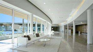 A modern hotel lobby with a curved ceiling, a seating area with a sofa and coffee table, and large windows offering a view of the outdoors. - The Anchor Troia River (Grandola)