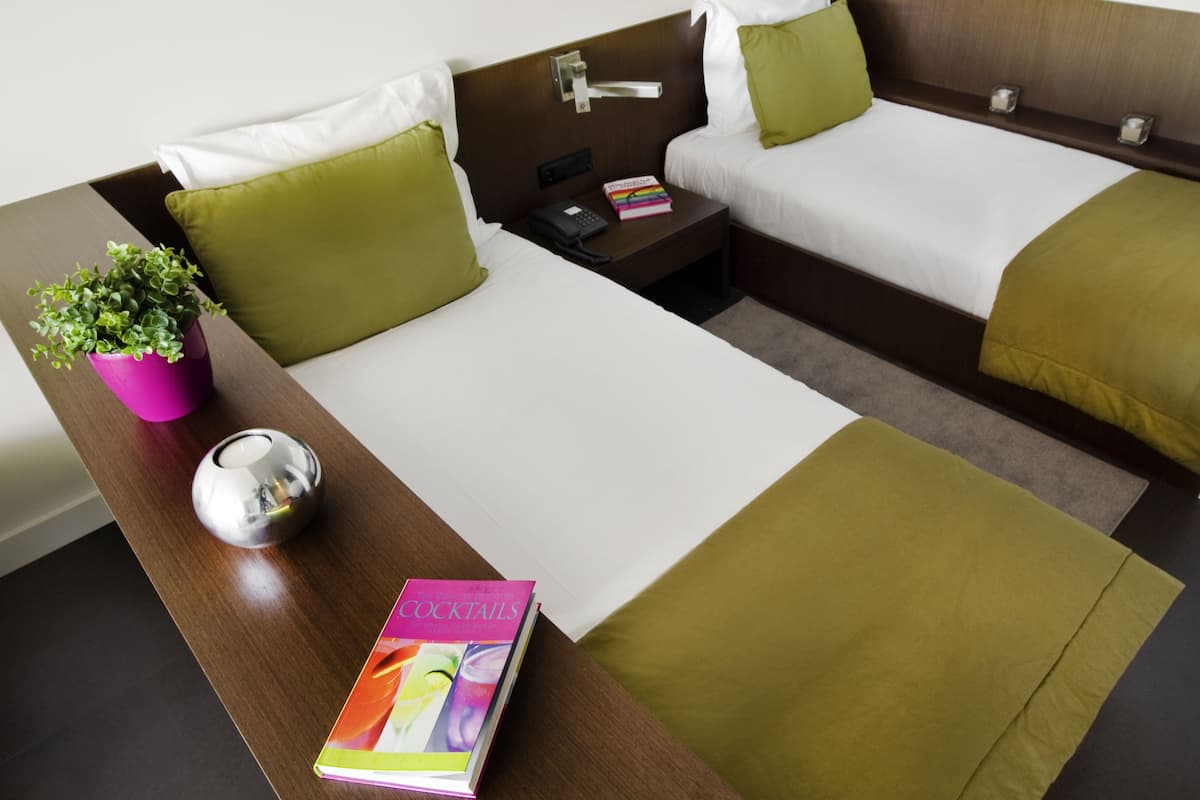 Habitación de hotel con dos camas, una mesita de noche, una planta en maceta y un libro titulado "The Art of Cocktails".