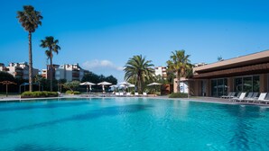 A clear blue swimming pool with lounge chairs and umbrellas, surrounded by palm trees and modern buildings. - The Anchor Troia River (Grandola)