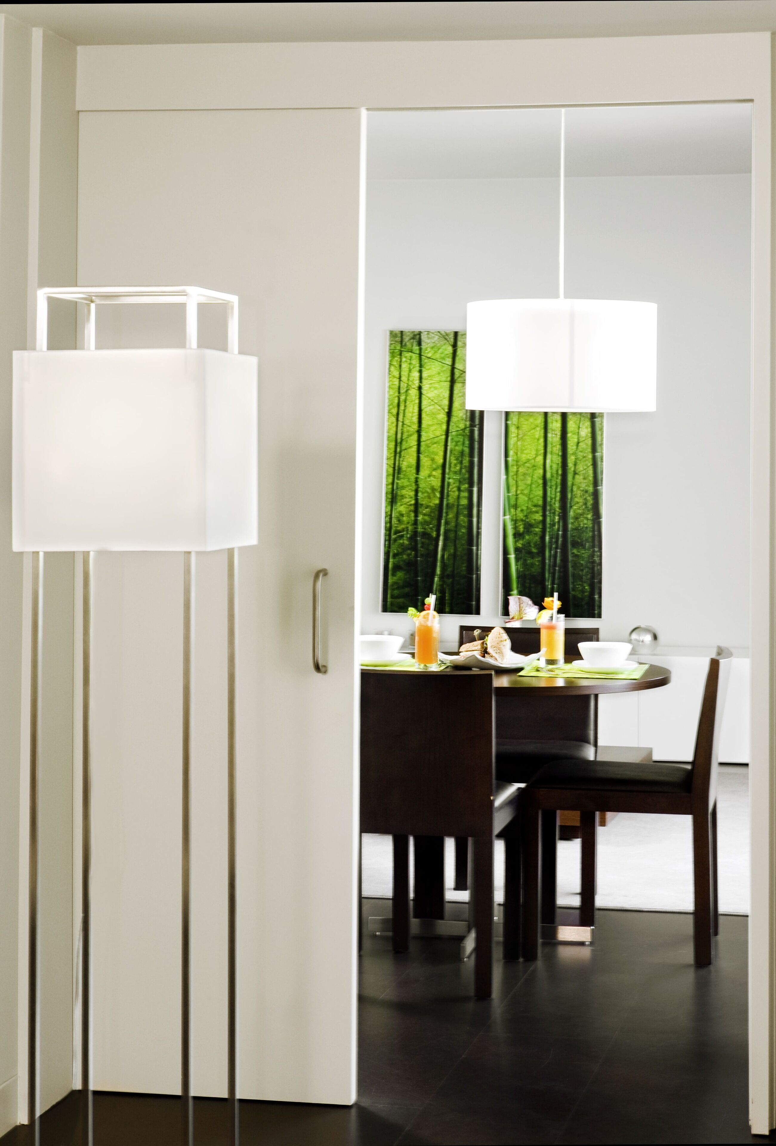 Un comedor moderno con una mesa blanca, sillas oscuras y un ventanal con vistas a árboles verdes.