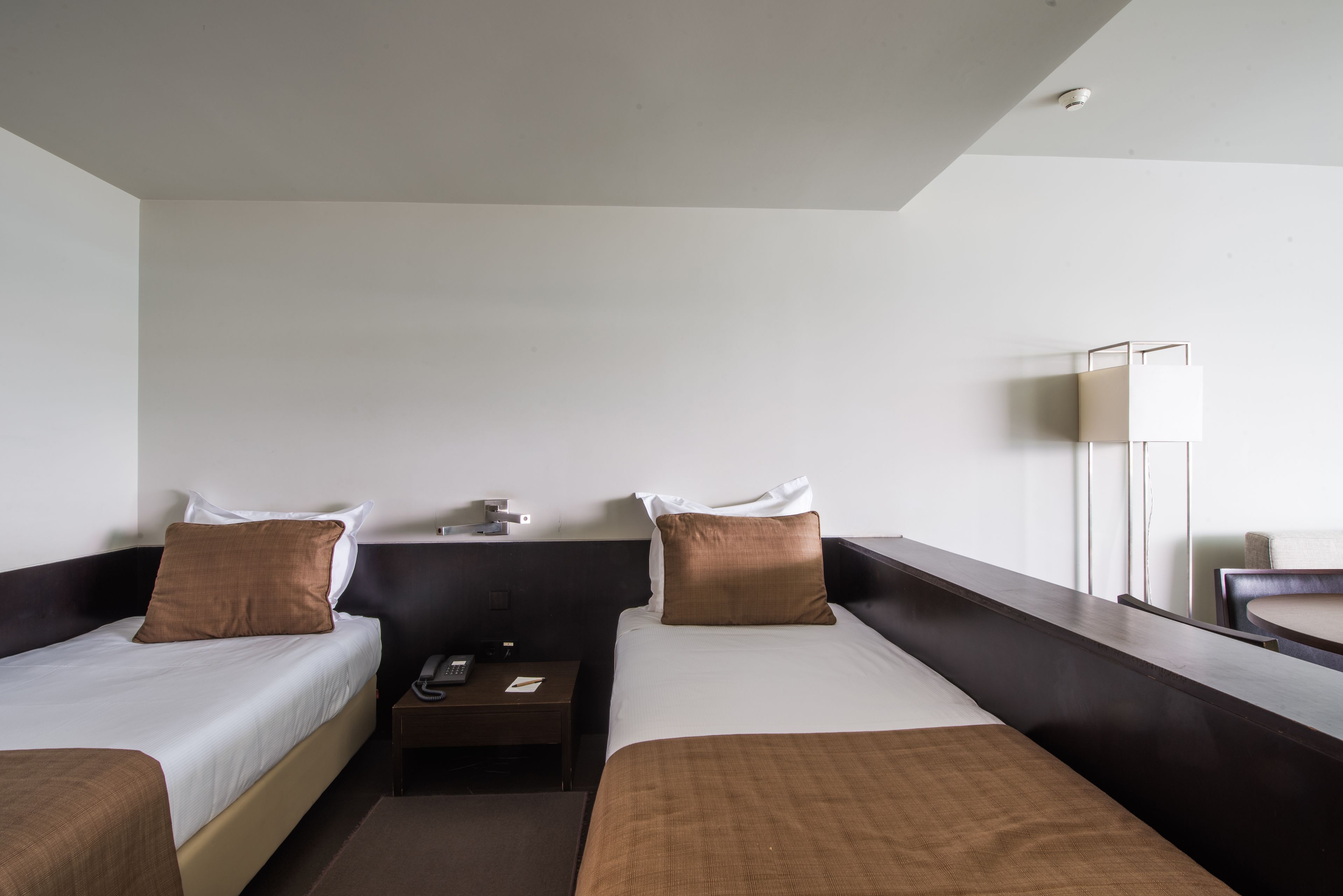 A hotel room with two beds, a bedside table with a phone, and a large window.