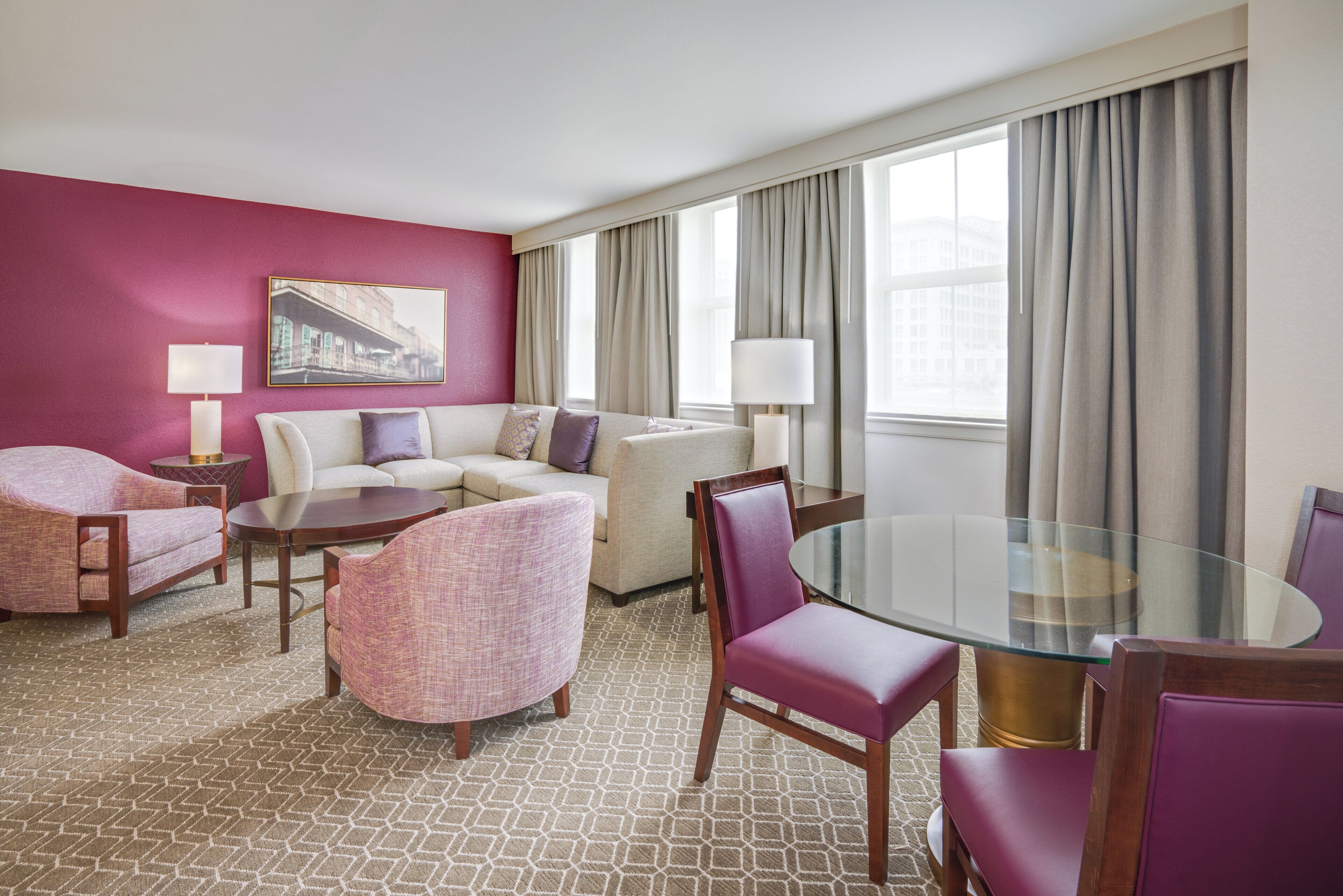 Une chambre d’hôtel avec un mur d’accent rouge, un ensemble de canapés, une table en verre et une vue sur la ville grâce à de grandes fenêtres.