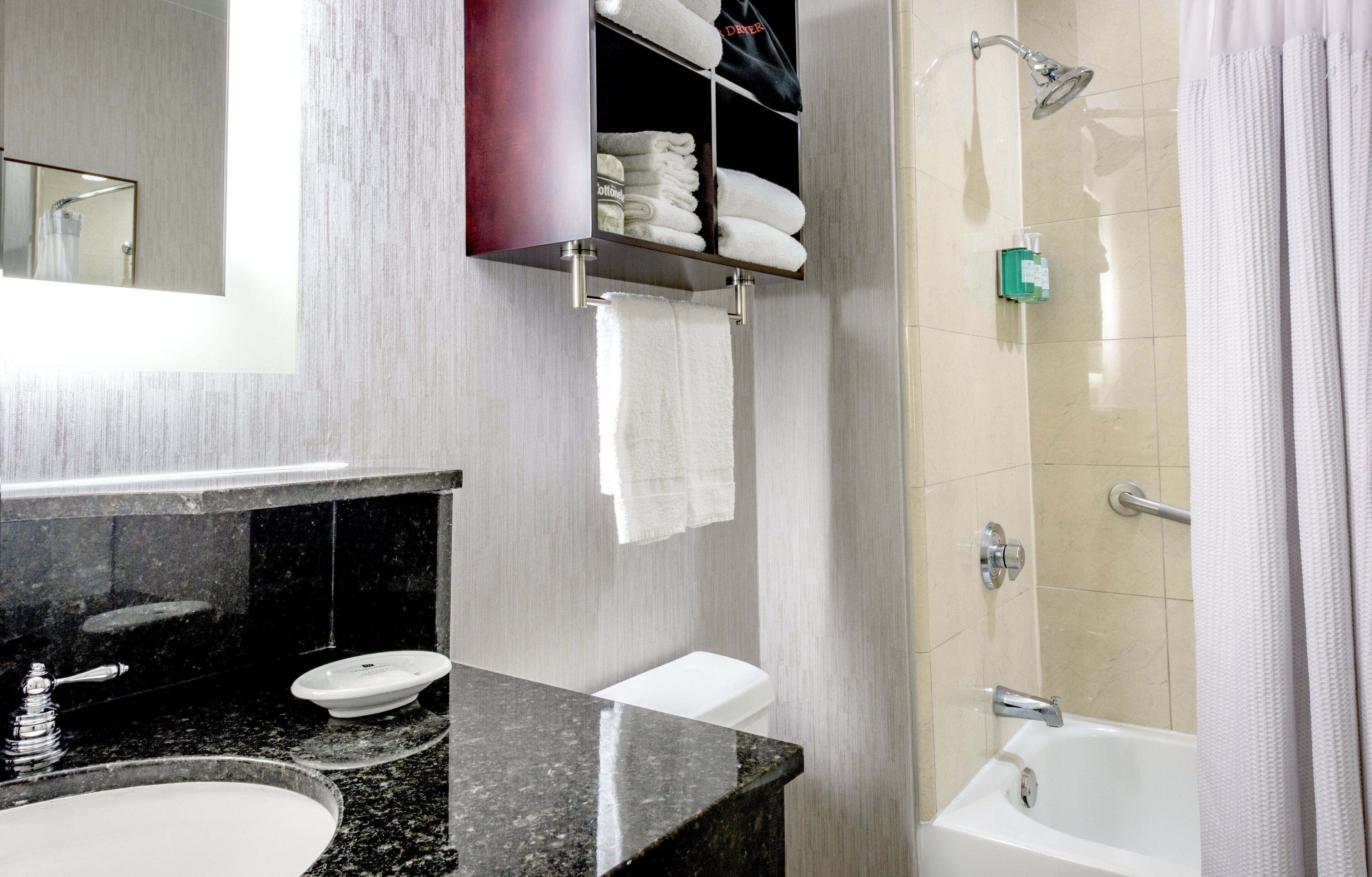 A modern bathroom with a granite countertop, a sink, a toilet, a shower with a glass door, and a towel rack with folded towels.