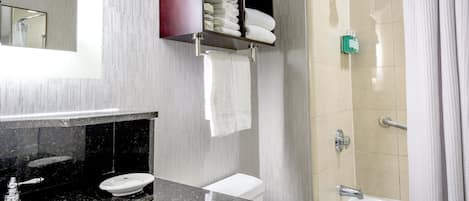 A modern bathroom with a granite countertop, a sink, a toilet, a shower with a glass door, and a towel rack with folded towels.