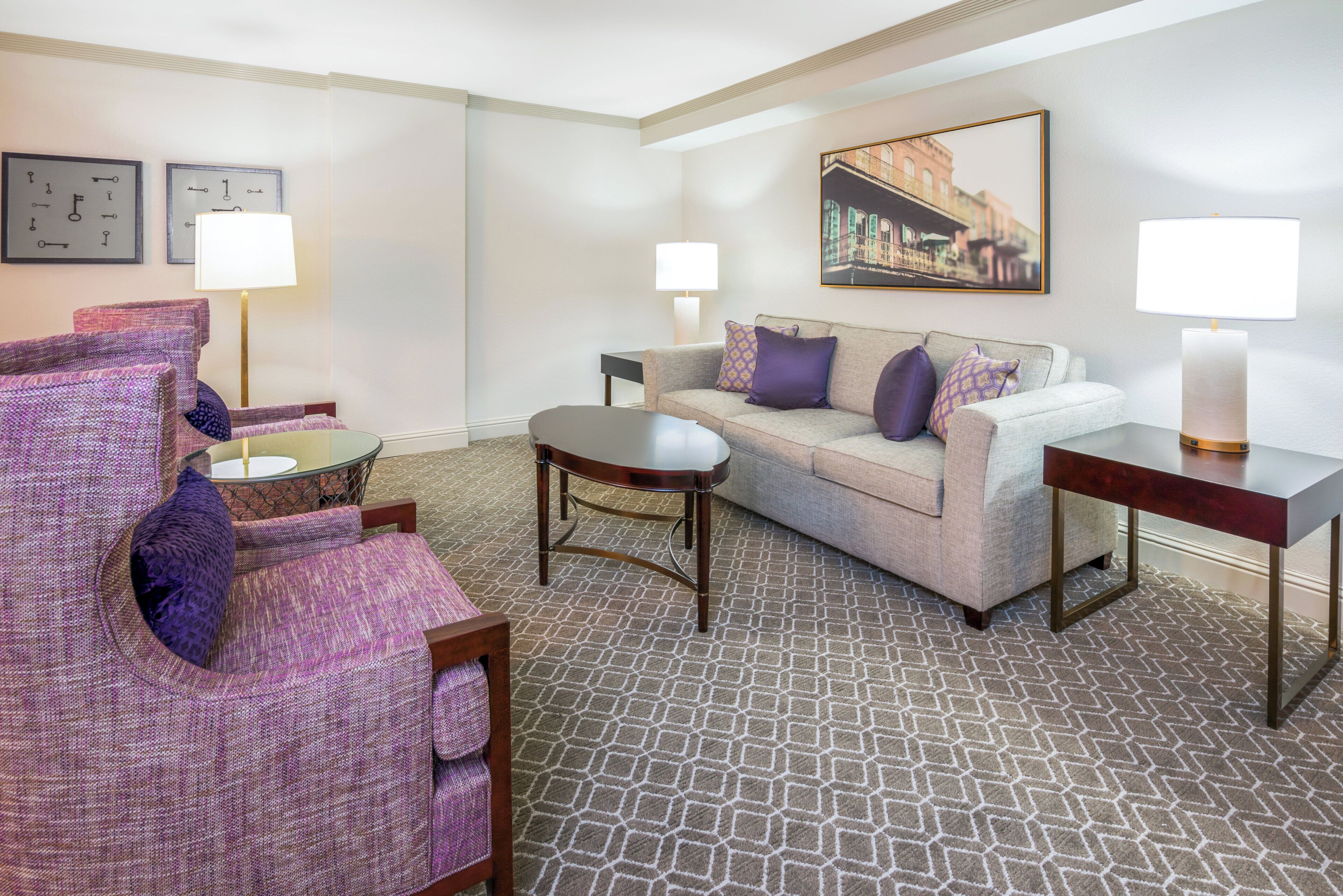 A hotel room with a sofa, armchair, coffee table, and lamps.