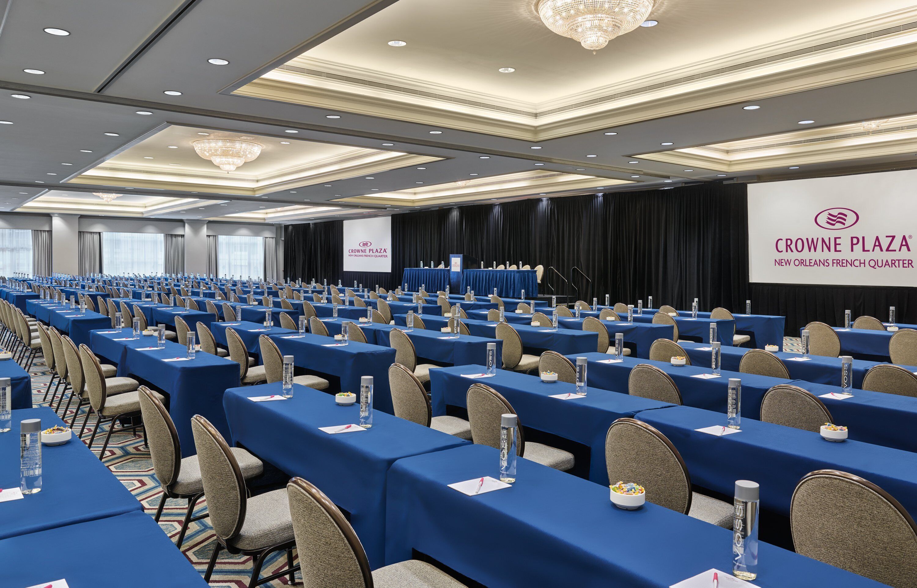 A conference room with rows of tables, chairs, and a stage with a podium.