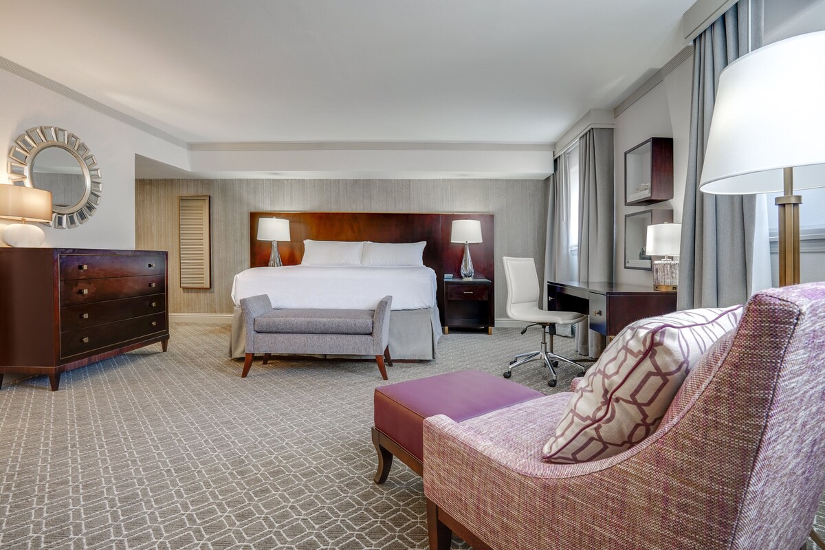 Een hotelkamer met een groot bed, een bureau, een stoel, een dressoir en een televisie.